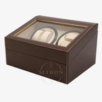 Brown leather watch box with glass top displaying two watches on a white background