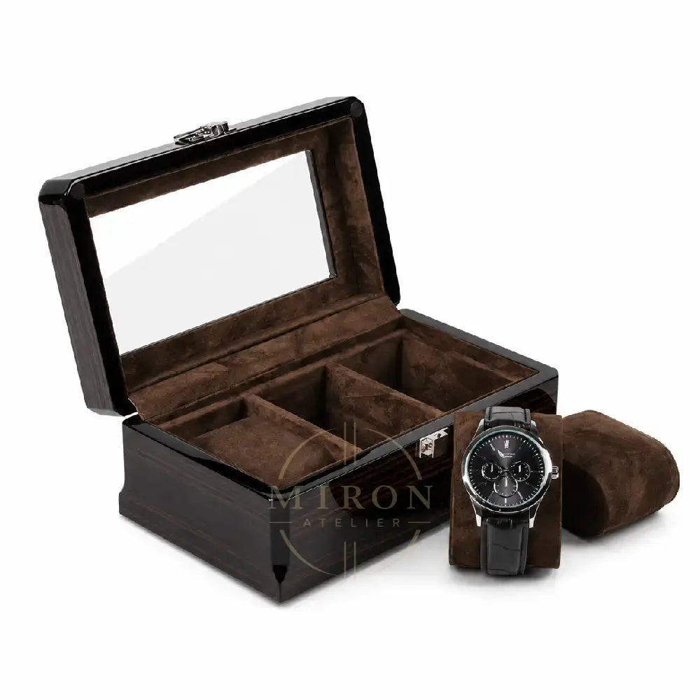 A dark wood watch box with a clear glass lid, brown velvet interior compartments, and a matching brown watch cushion holding a black wristwatch, shown on a white background.