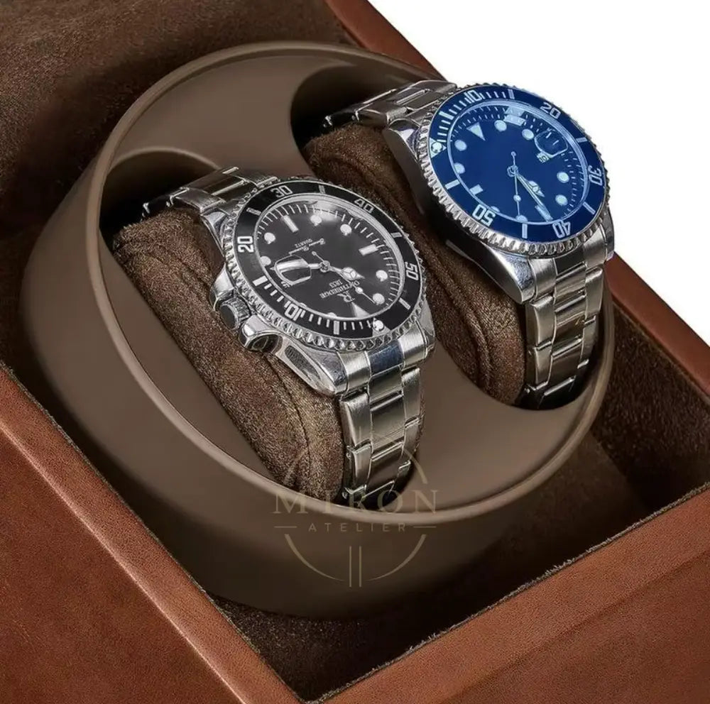 Close up of two watches, one with a black face and silver band, the other with a blue face and silver band, in a brown watch winder box.