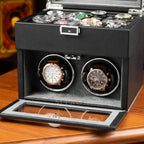 Black watch winder box with two rotating watch cases on a wooden surface