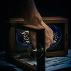Hand opening a wooden watch winder box containing two watches with blue accents