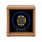 A luxury watch winder featuring a medium brown wood-grain frame and a black interior with a glowing blue circular light. A gold and black chronograph watch is displayed inside the center.