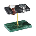 A watch display stand with a black faux-croc leather top, a gold metal stem, and a green marble base, shown holding two watches on a white background.