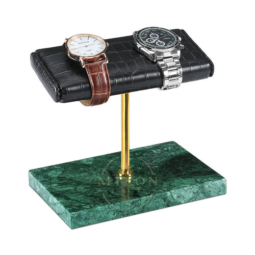 A watch display stand with a black faux-croc leather top, a gold metal stem, and a green marble base, shown holding two watches on a white background.