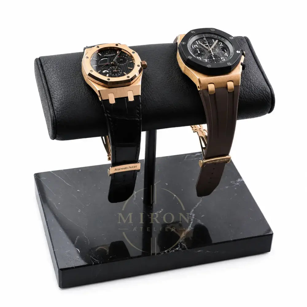Two gold luxury watches Audemars Piguet on a black marble watch stand with a white background