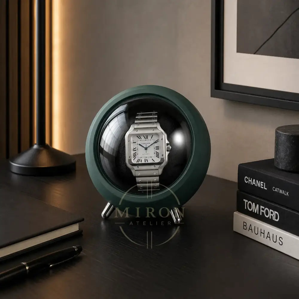 Cartier watch in a green watch winder on a desk with books and a lamp.