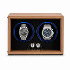 A wooden dual watch winder with a medium brown wood-grain finish, black textured interior, and two circular watch slots illuminated by blue LED lights. Two stainless steel watch dials are displayed inside as demonstration props.