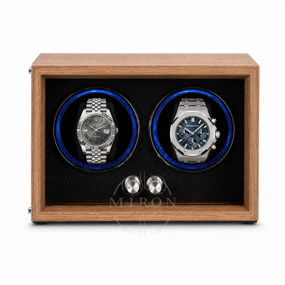 A wooden dual watch winder with a medium brown wood-grain finish, black textured interior, and two circular watch slots illuminated by blue LED lights. Two stainless steel watch dials are displayed inside as demonstration props.