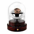 Rose gold watch inside a clear glass dome on a wooden base with a white background. Watch Winder Wood Finition