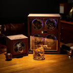 Wooden watch winder with two rolex watches and a glass of whiskey on a wooden surface.