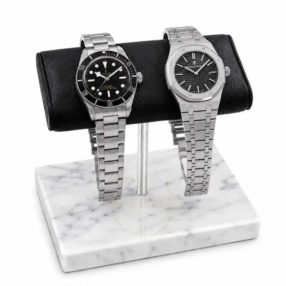 Two silver luxury watches Tudor and Audemars Piguet on a marble watch stand with a white background